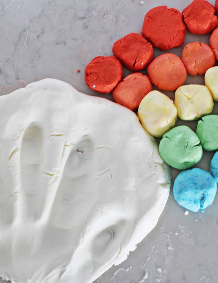 Handprint in white cloud dough next to balls of homemade dough in rainbow colors.