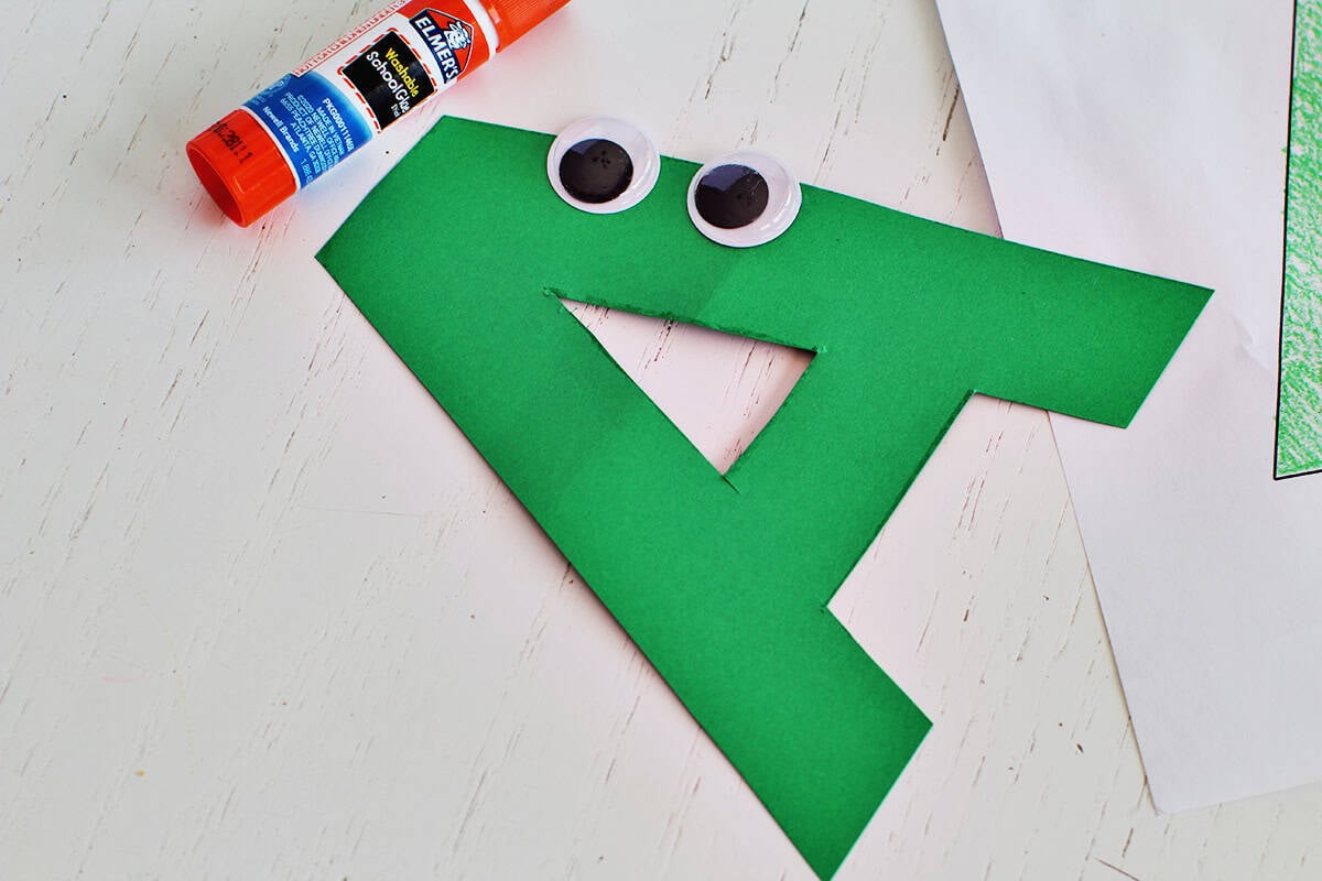 Googley eyes being added to a cut out letter 'A'. 