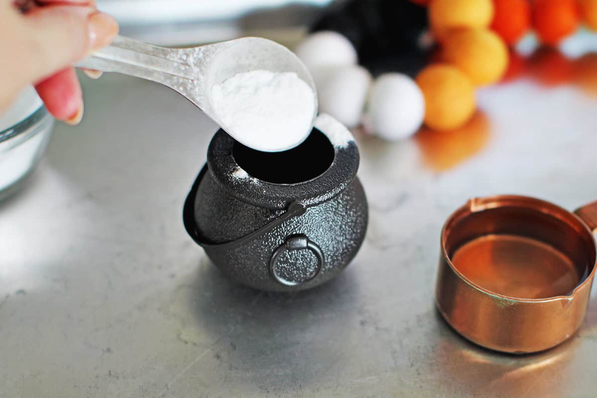 Baking soda being added to a small plastic cauldron.