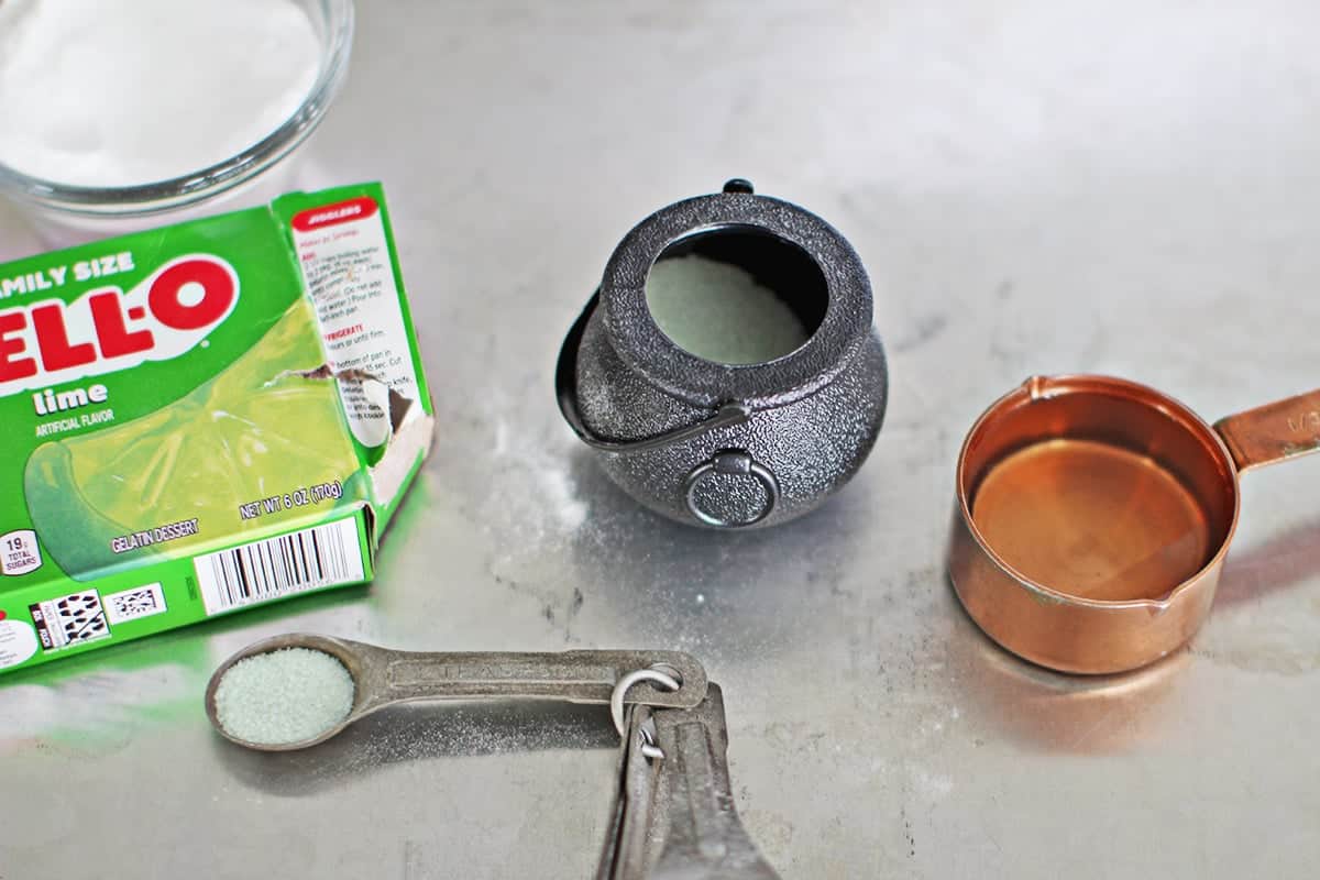 green jello box next to a plastic cauldron being added to the mixture.
