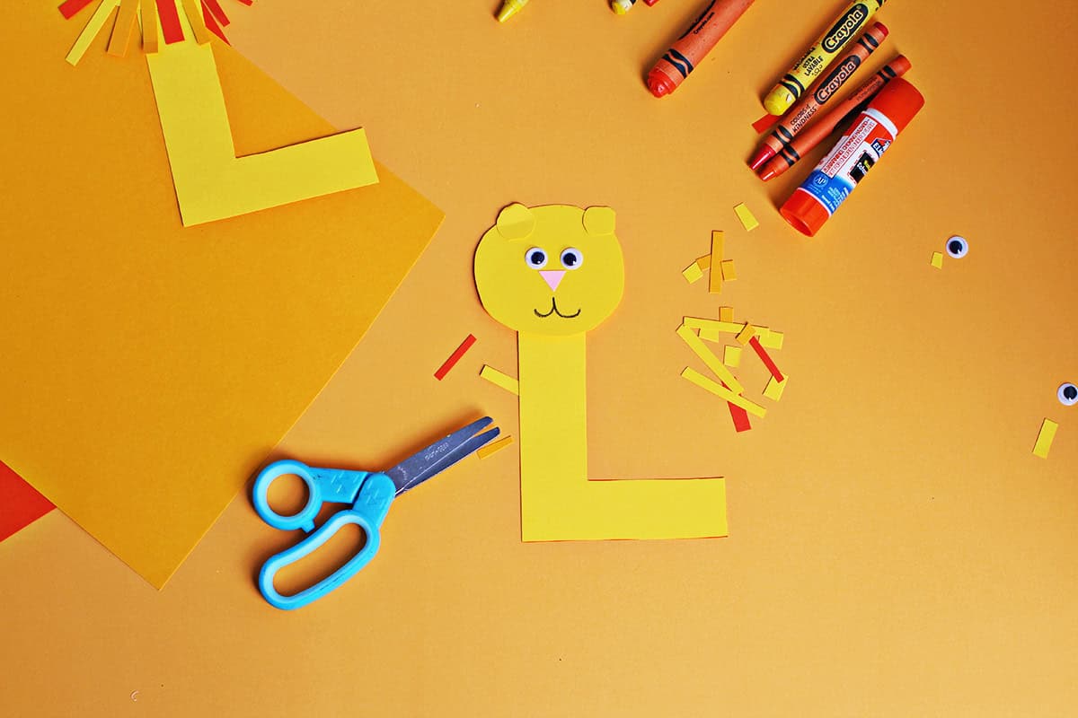 Googley eyes, a cut out pink nose and drawn on whiskers added to a round yellow circle glued onto a cut out cardstock yellow L making a lion.