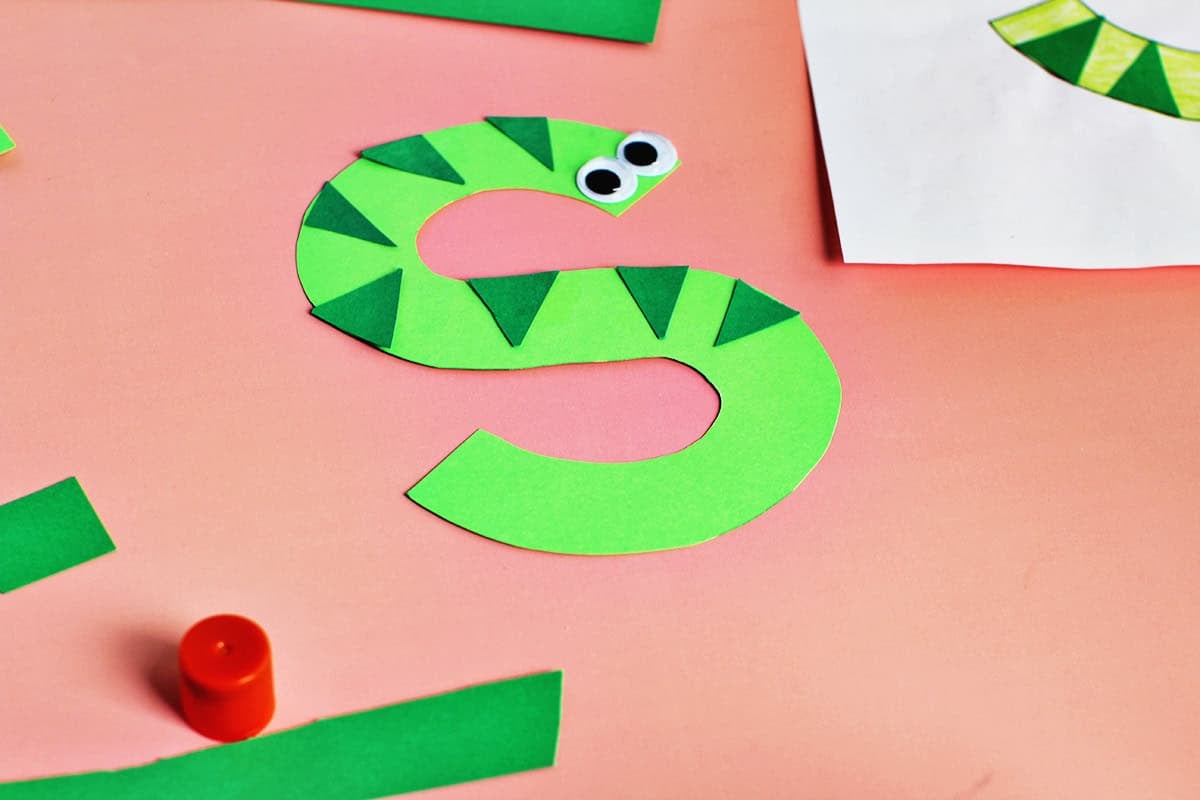 Add googley eyes to paper snake craft.
