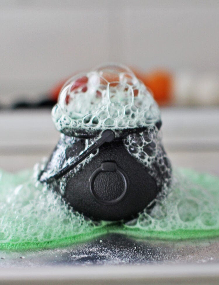 Baking soda, vinegar and green jello powder combined in a small plastic cauldron for a Halloween science experiment.