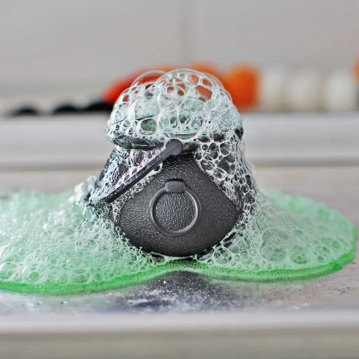 A plastic cauldron with baking soda and vinegar combined so that it bubbles out of the cauldron onto a baking tray.