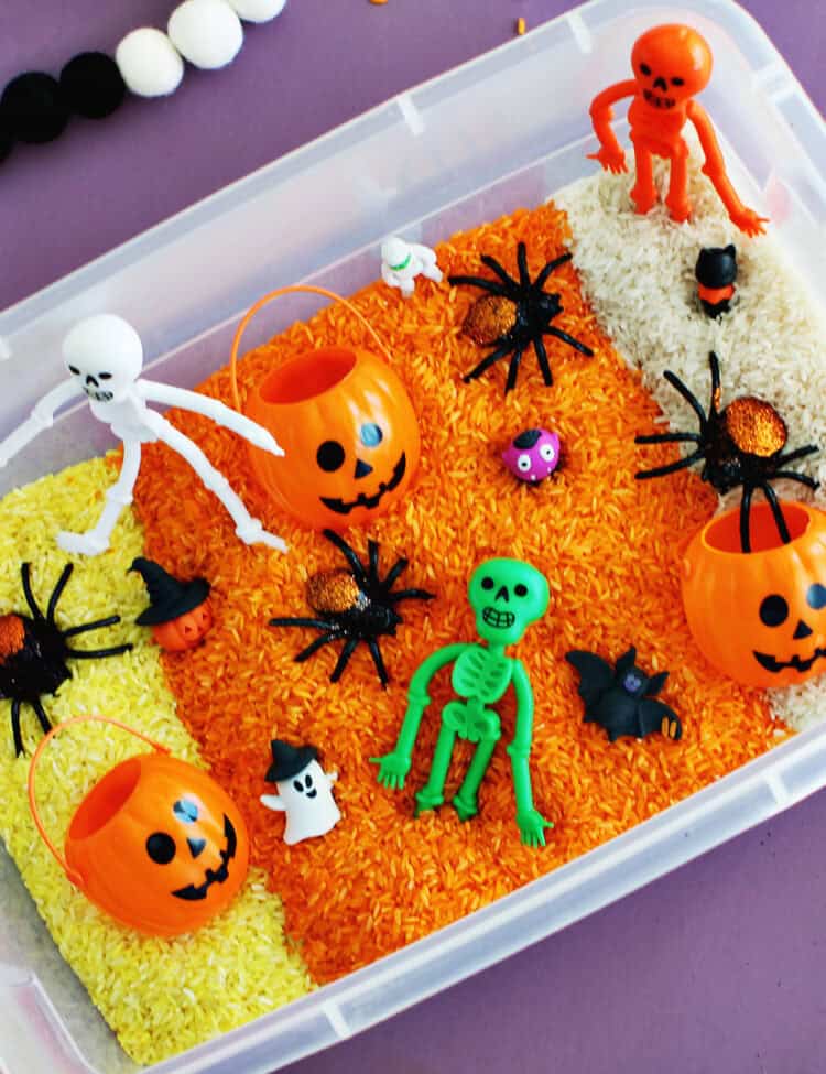 Halloween sensory bin with rice dyed yellow, orange and white and filled with Halloween toys.