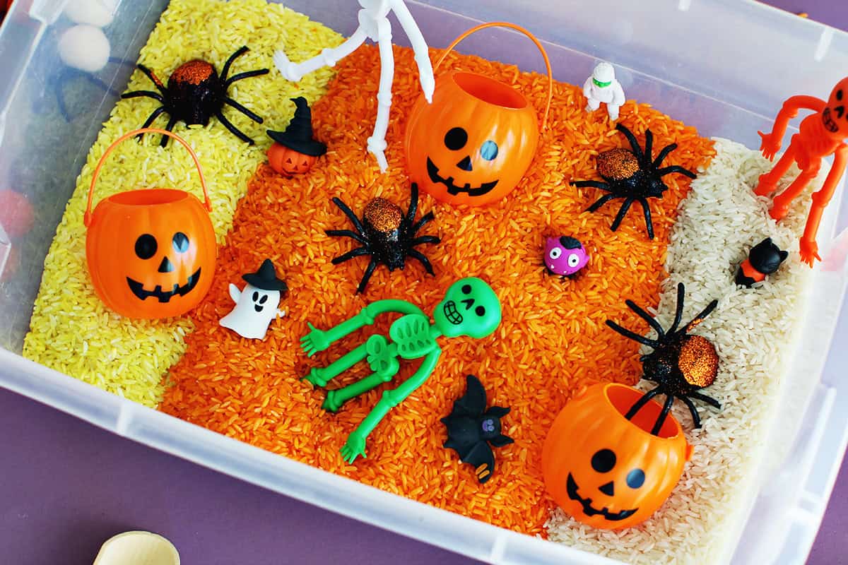 Halloween sensory bin with rice dyed yellow, orange and white and filled with Halloween toys.