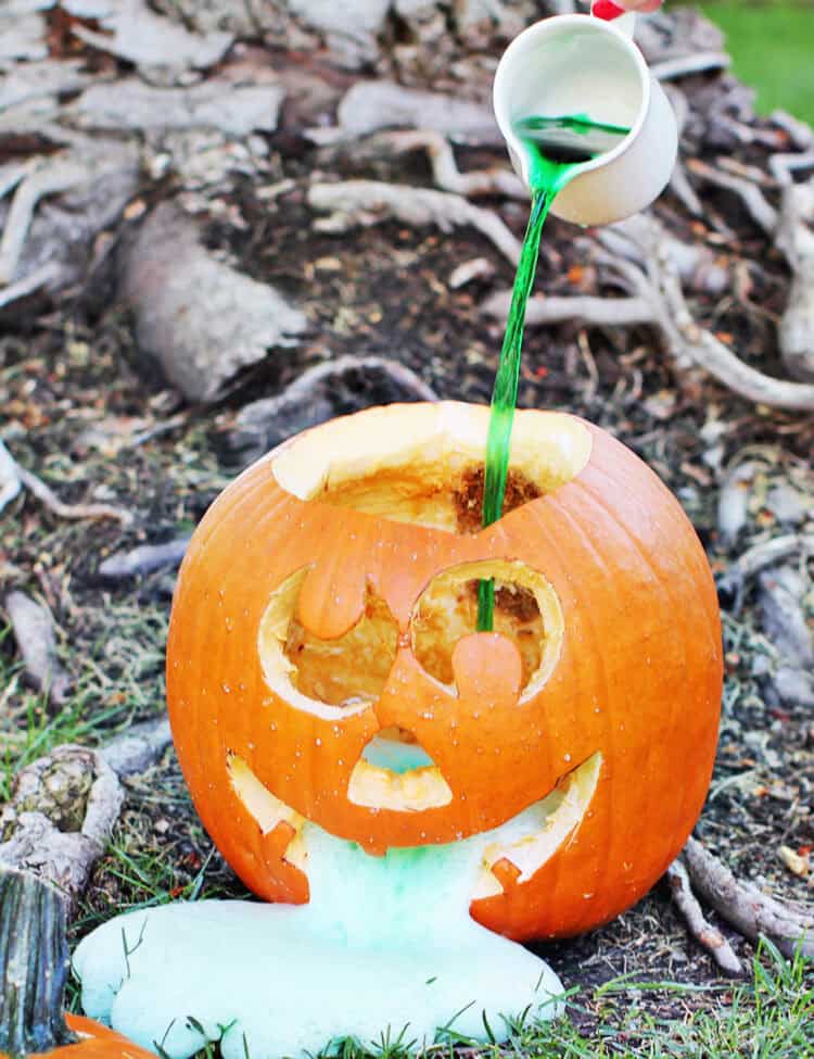 vinegar and food coloring solution being poured into a carved pumpkin.