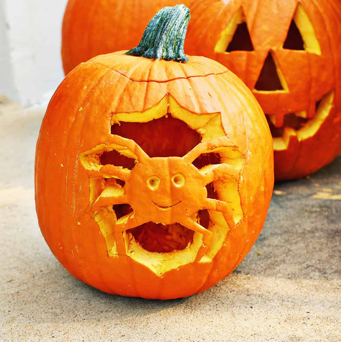 pumpkin carved with a spider in a web next to a traditionally carved pumpkin.