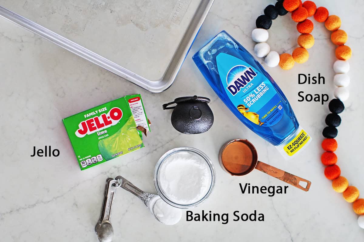 Green jello, dawn dish soap, baking soda, vinegar and a small plastic cauldron on a countertop. 