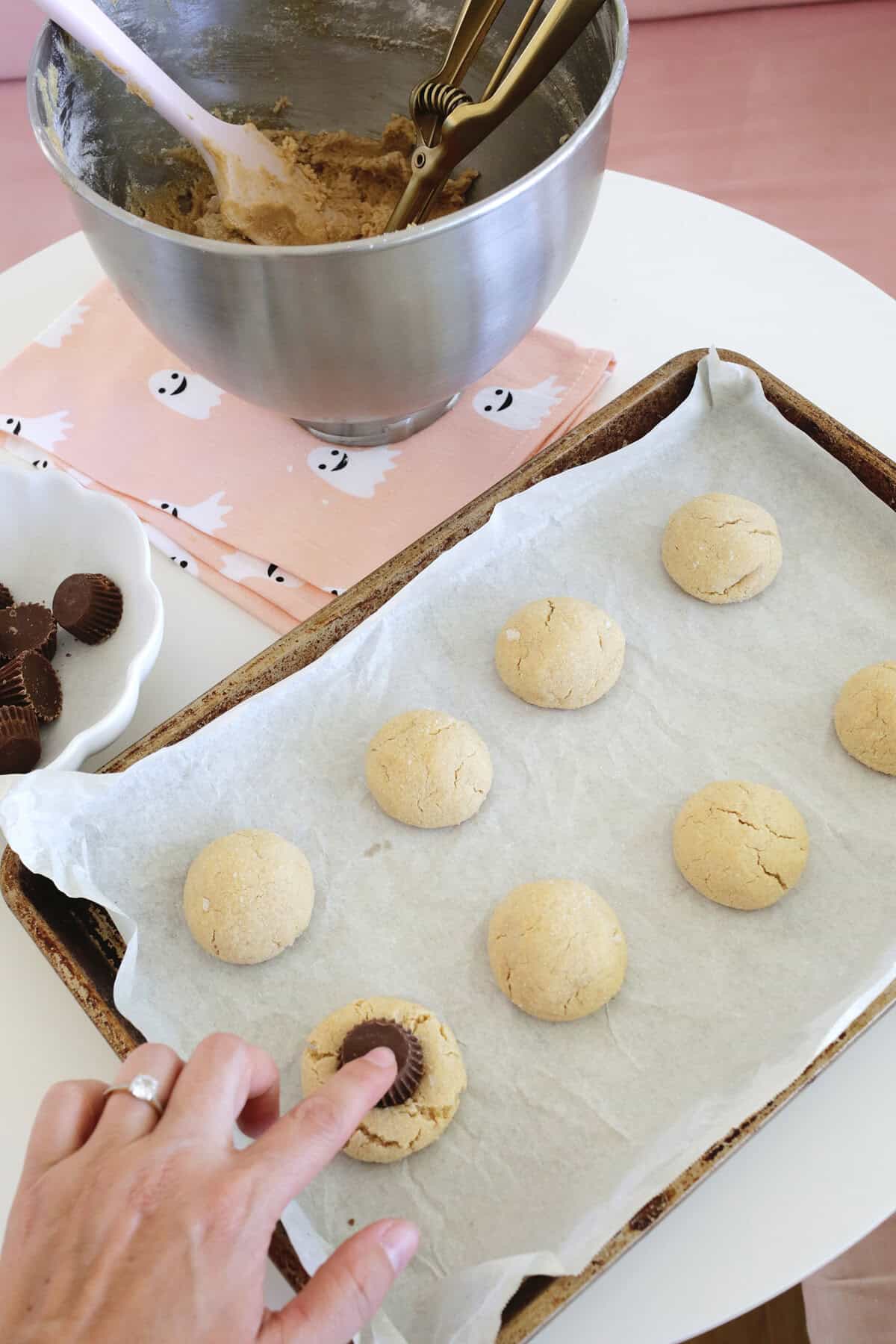 hand pressing a reeses candy into a baked peanut butter cookie.