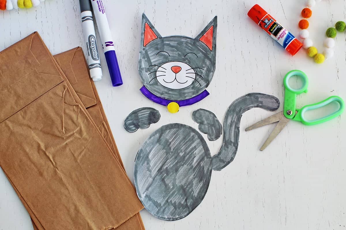 Cut out paper in a cat shape to be glued onto a paper bag to make a puppet.