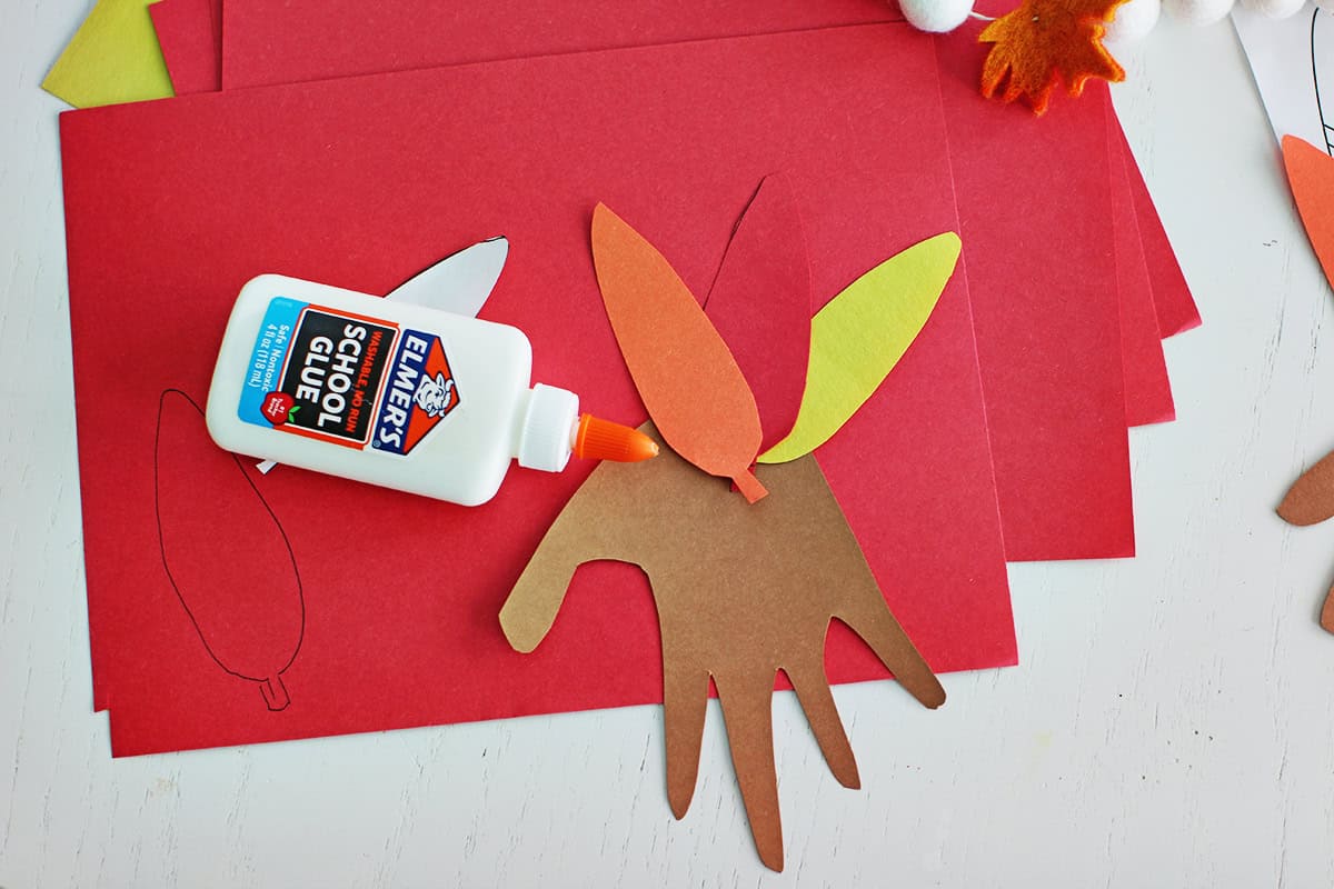 Construction paper feathers being glued onto a traced and cutout handprint.