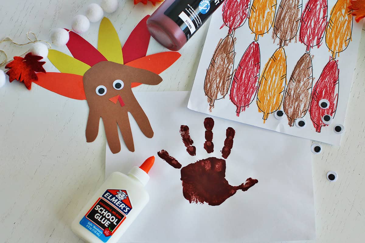 Painted brown handprint on a piece of paper next to colored in turkey feathers and a turkey handprint craft.