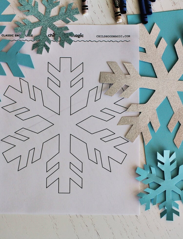 printed paper with snowflake shape on it next to cut out snowflakes.