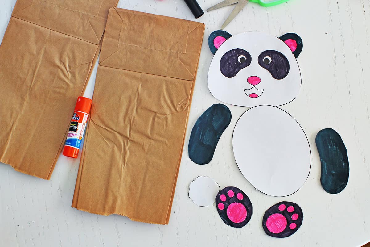 Paper bags next to a gluestick and cut out panda pieces.