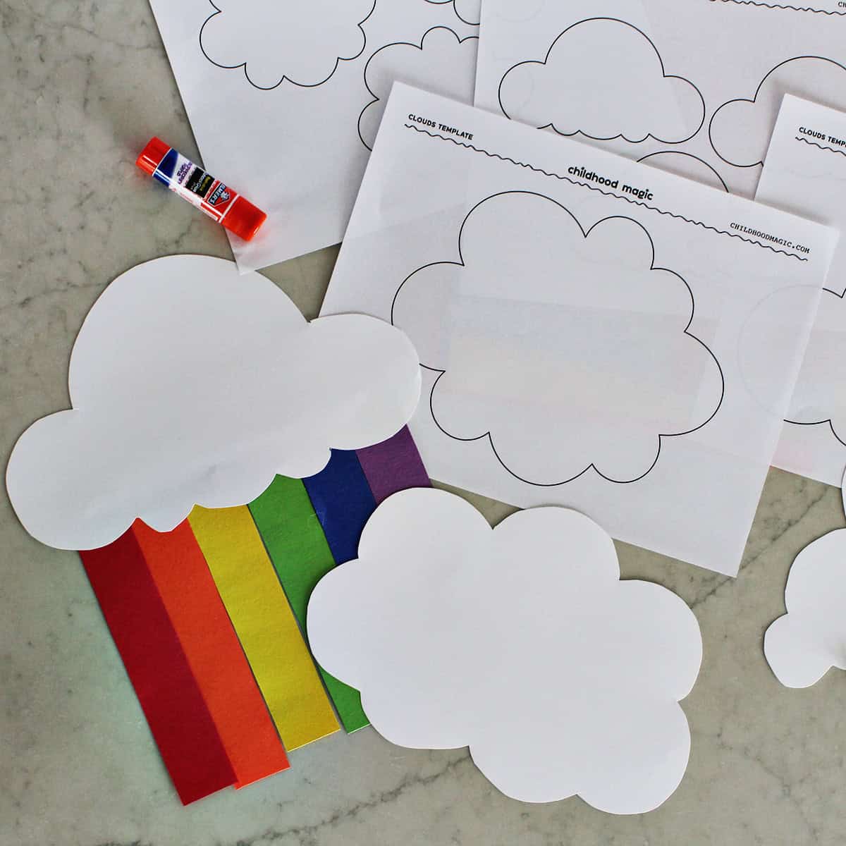 Cloud cutout with paper strips to make a rainbow next to printable pages of clouds by a gluestick.