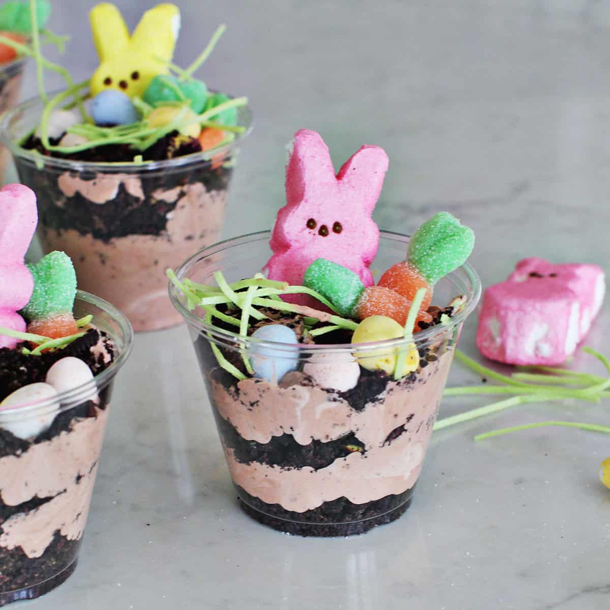 Clear cup filled with chocolate pudding mixture, crushed oreos and Easter candy including a pink Peep.
