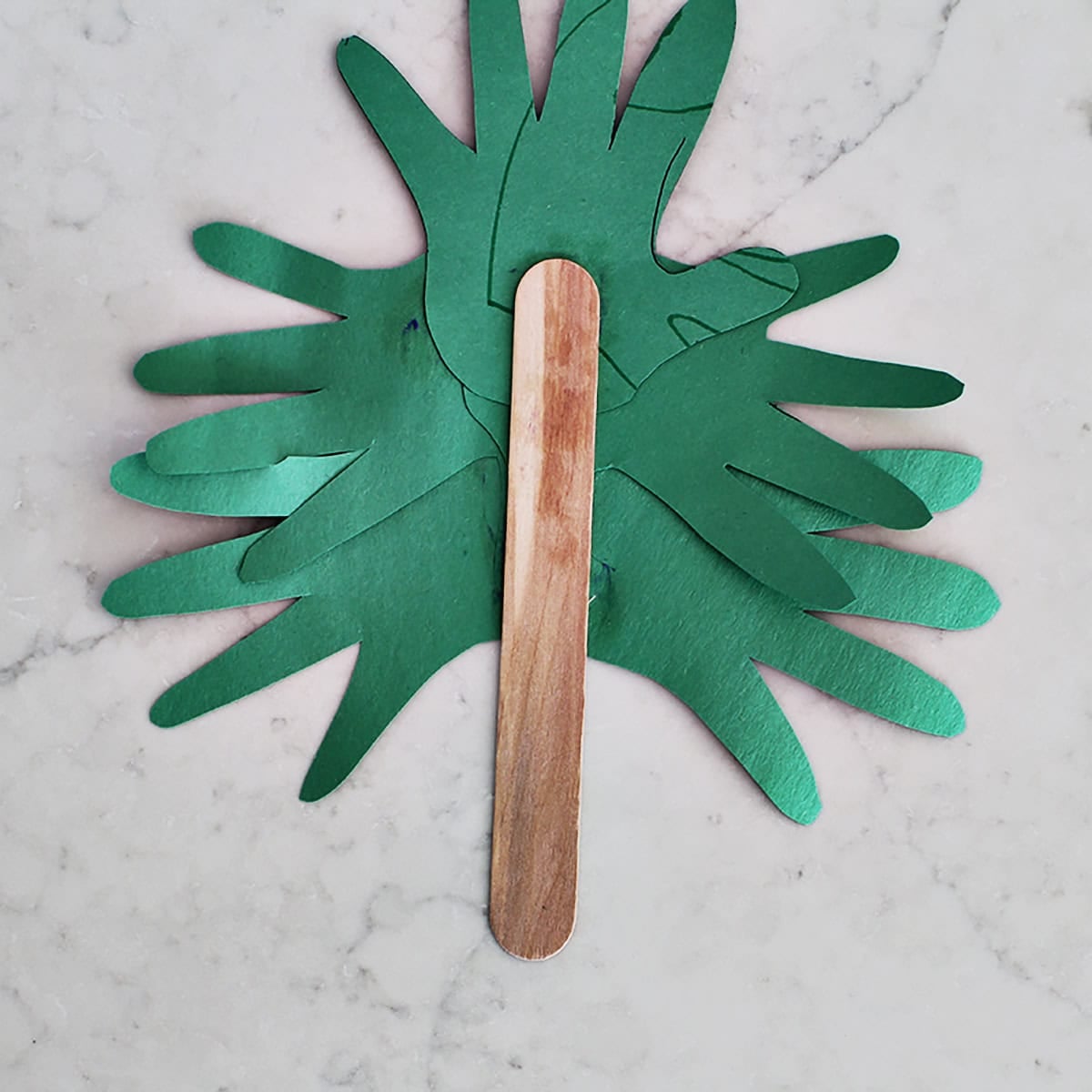 Large popsicle stick being glued to green construction paper handprints.
