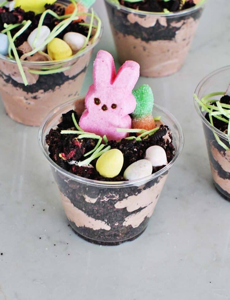 Clear cup filled with chocolate pudding mixture, crushed oreos and Easter candy including a pink Peep.