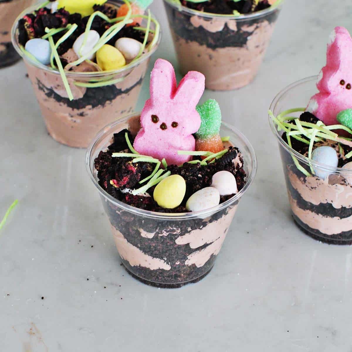 Clear cup filled with chocolate pudding mixture, crushed oreos and Easter candy including a pink Peep.