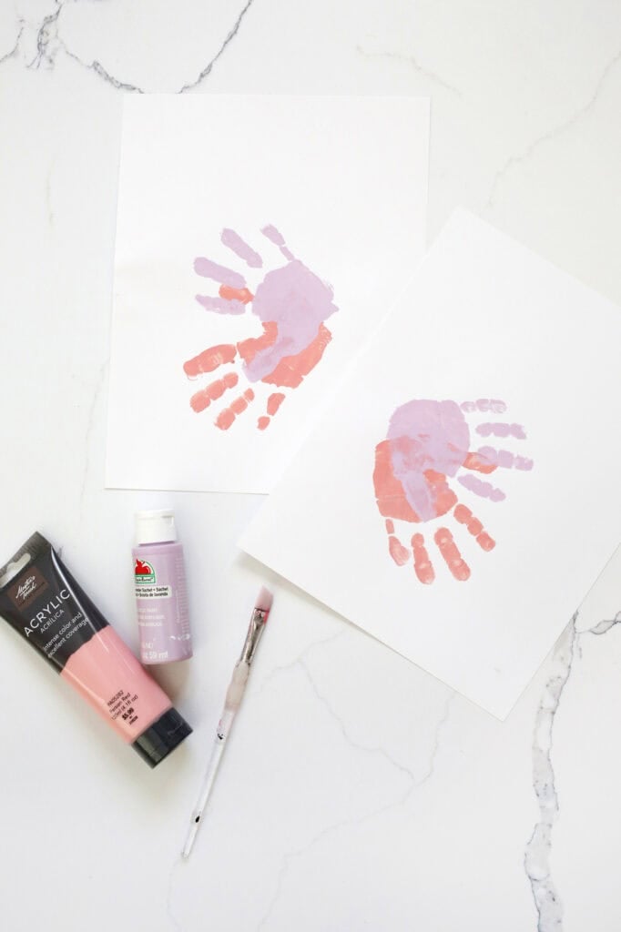 handprints being painted to make a butterfly next to acrylic paint and a paintbrush.