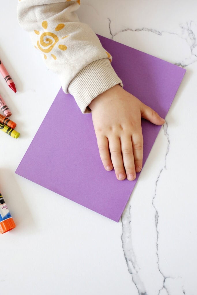 Child's hand being traced onto a folded piece of purple paper on a counter.