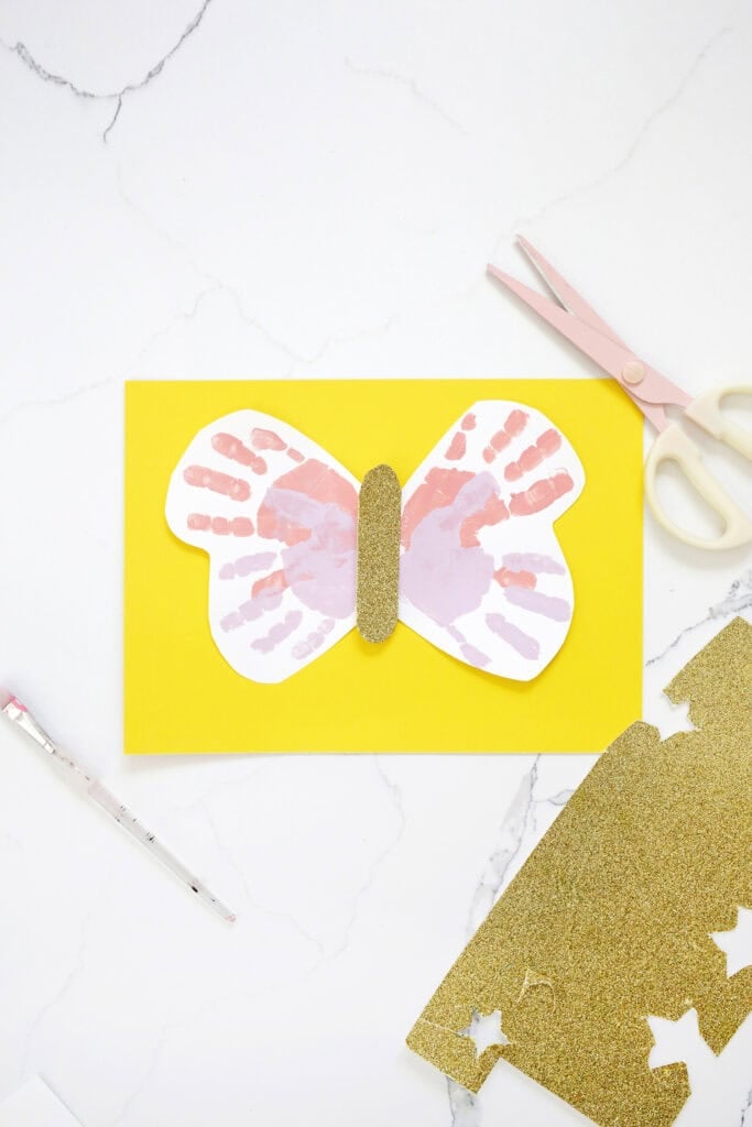 Handprints made into butterfly wings gleud onto a piece of yellow paper.