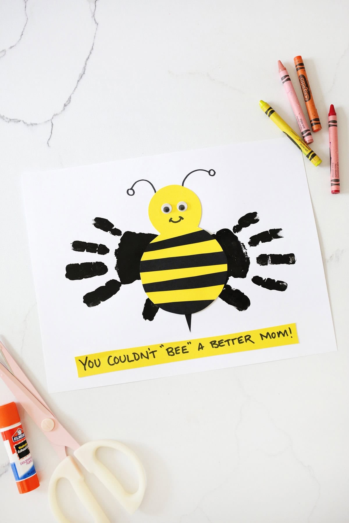 Handprint bee Mother's Day craft on a counter next to crayons.