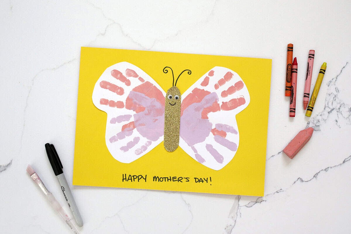 Handprint Mother's Day craft butterfly next to crayons, a sharpie and a paintbrush.
