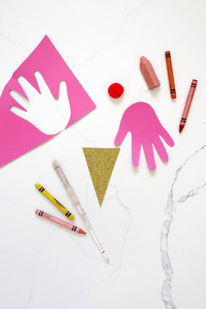 Pink construction paper handprint next to crayons and a paintbrush.