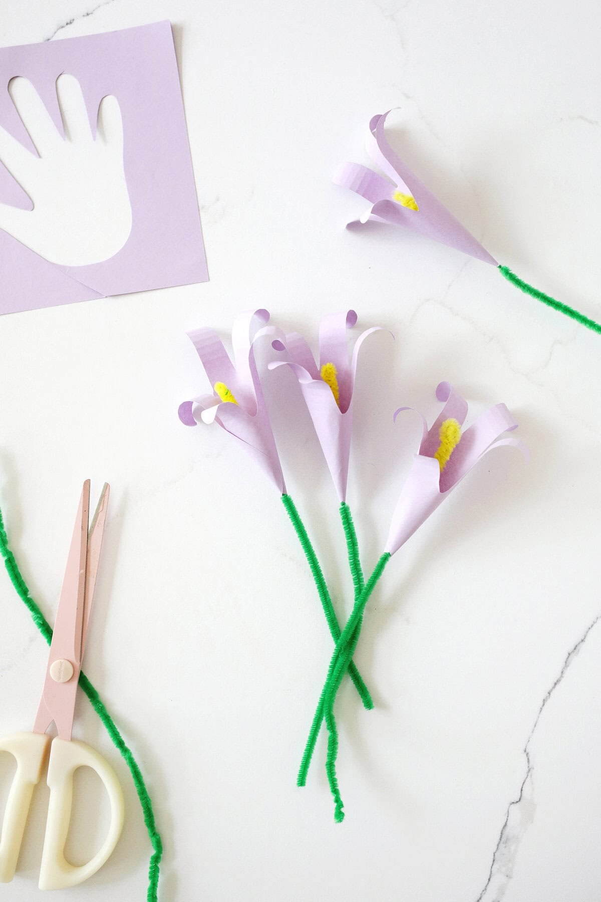 Handprint Mother's Day craft lilly flower with a green pipe cleaner stem on a counter next to a pair of scissors.