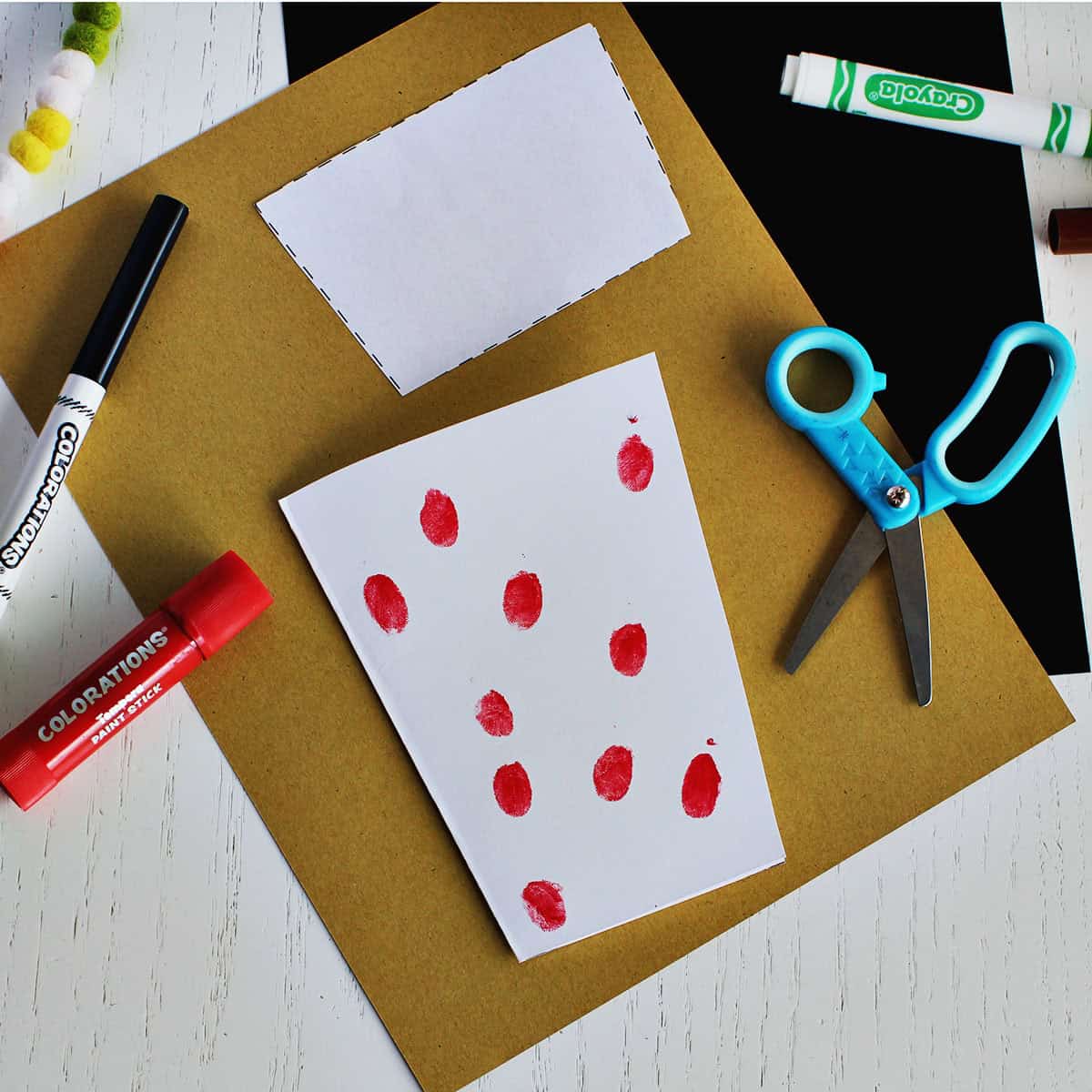 Red painted fingerprints on a coffee cup shaped card next to kids scissors.