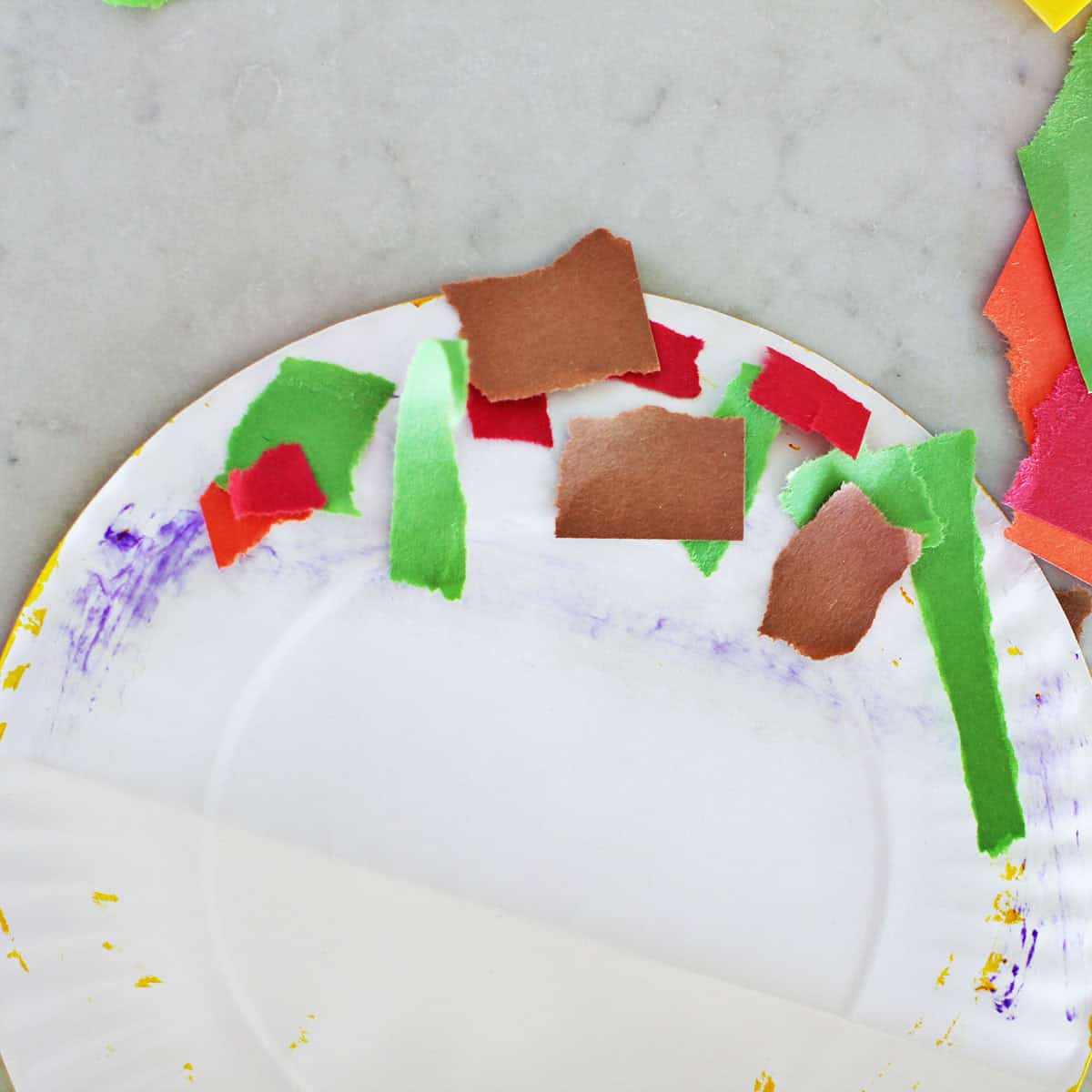 Piece of green, brown and red construction paper glued onto a paper plate that's been folded in half.
