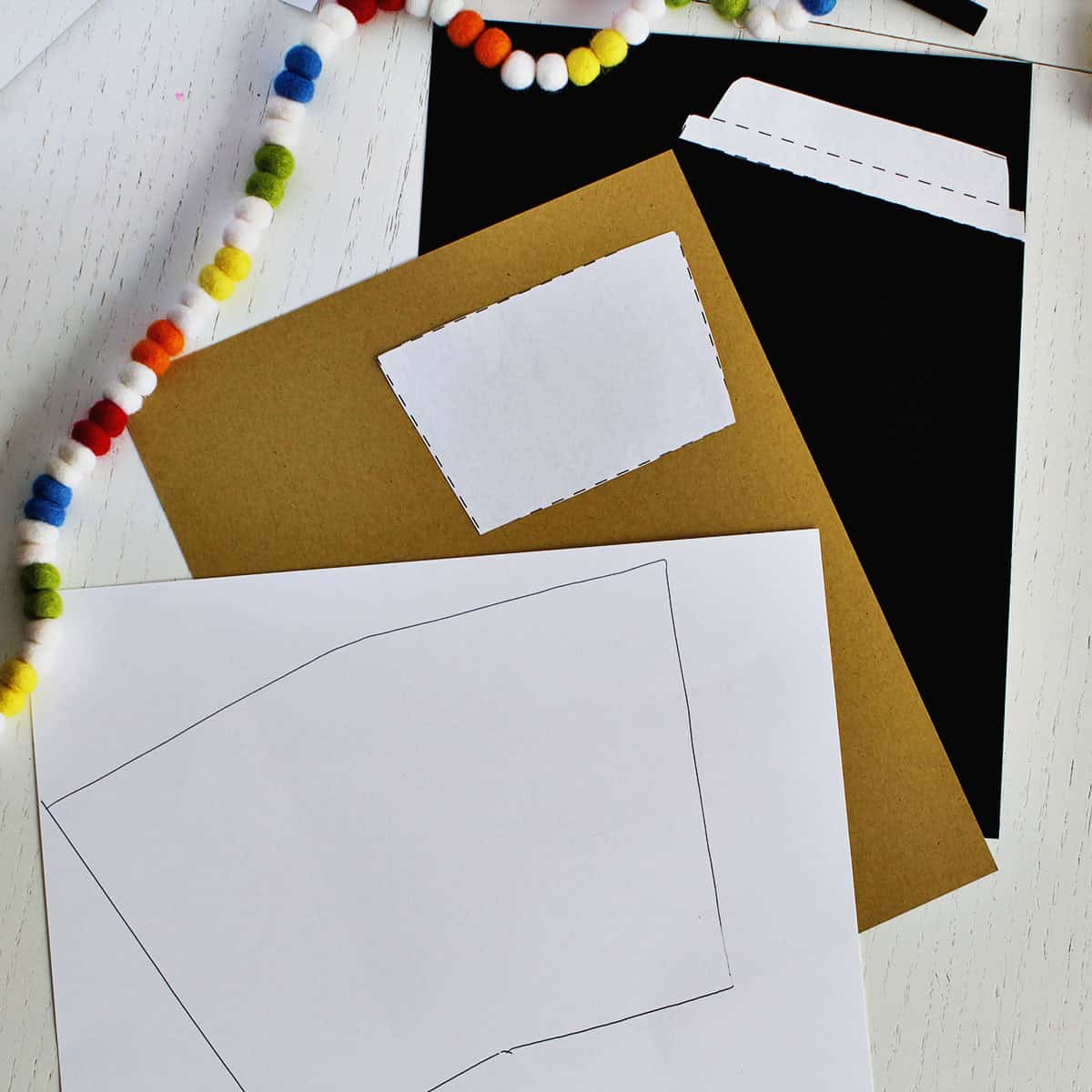 outline of a card on white cardstock next to tan and black cardstock paper.