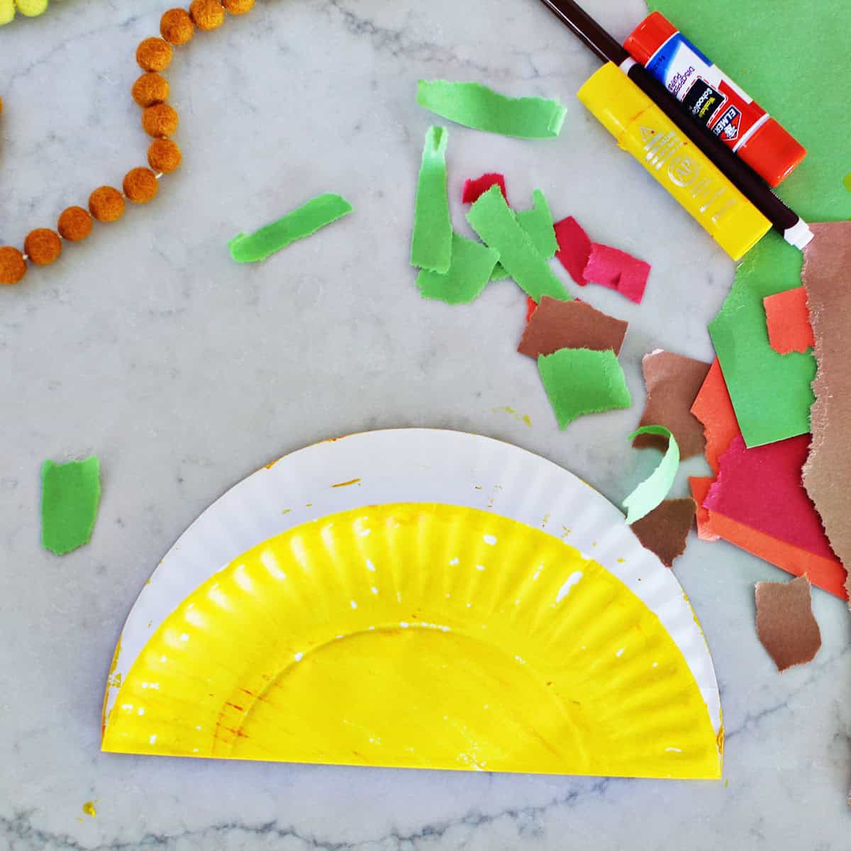 A paper plate painted yellow and folded 2/3 of the way closed.