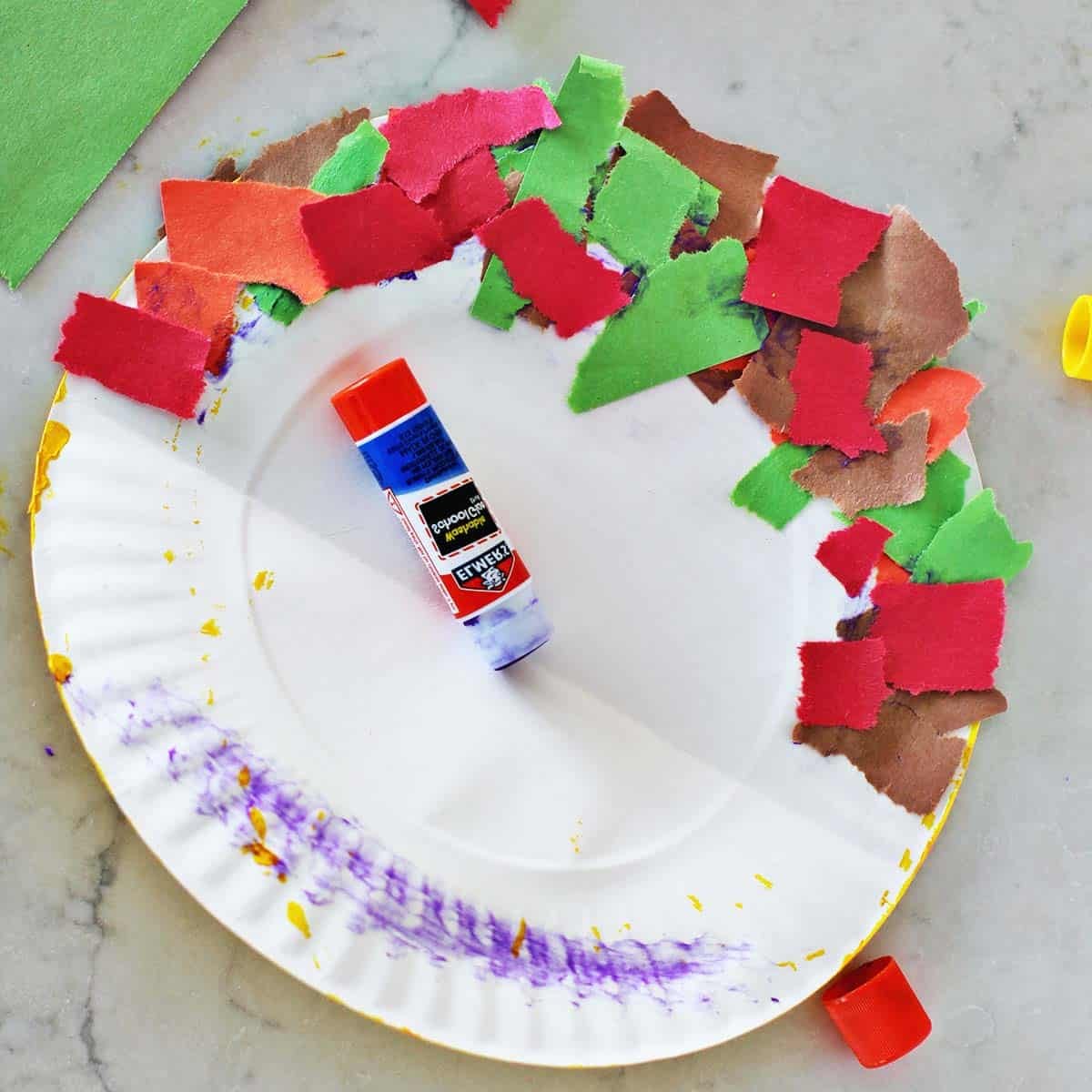 Piece of green, orange, brown and red construction paper glued onto a paper plate that's being folded in half and glued together.