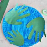 green paper handprints on a painted blue paper plate to look like the planet Earth.