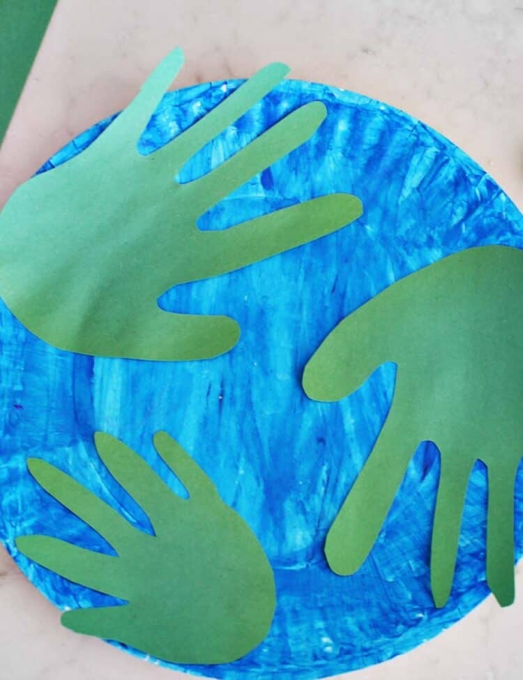 green paper handprints on a painted blue paper plate to look like the planet Earth.