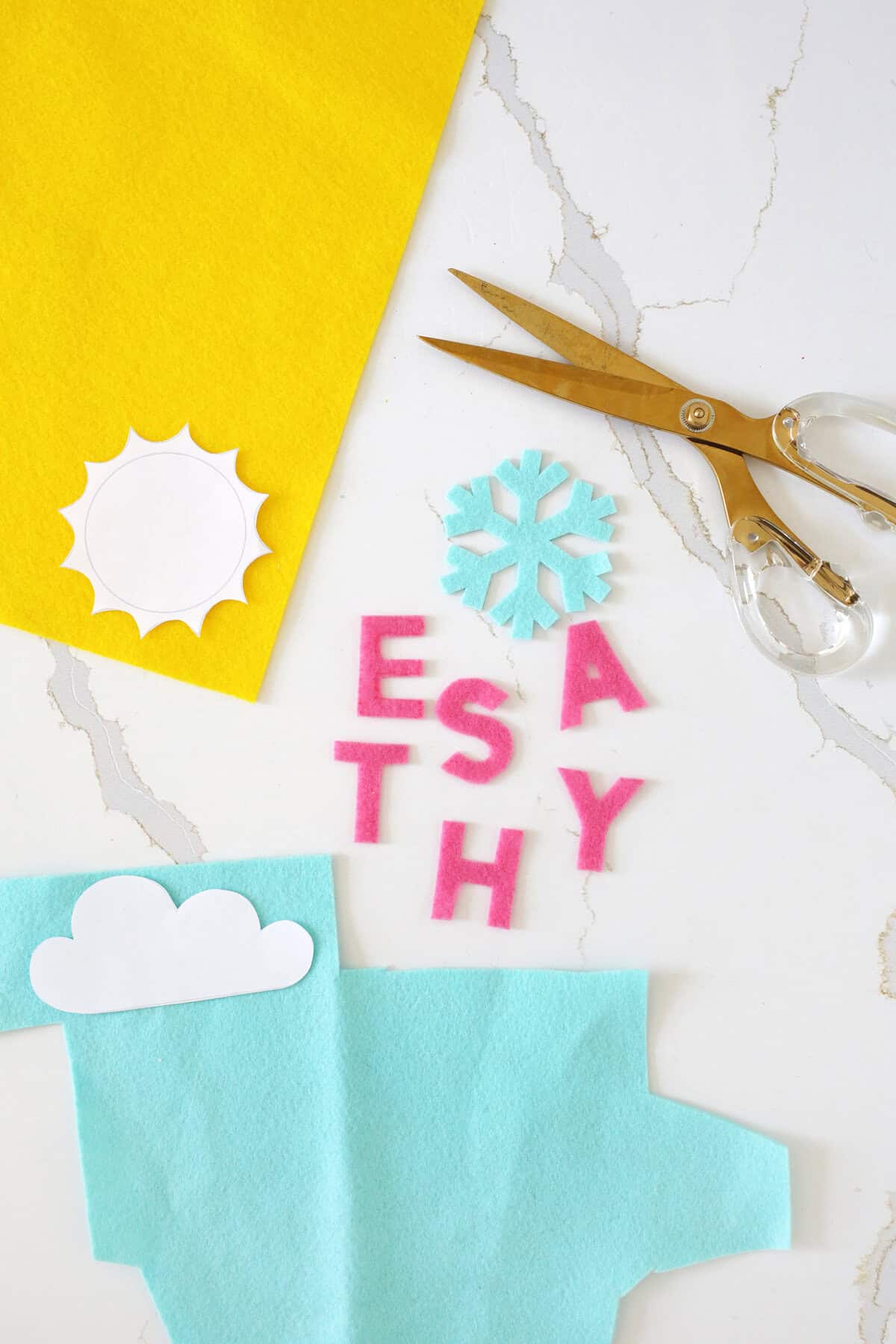 Felt letters and weather symbols cut out of blue, pink and yellow felt on a counter.