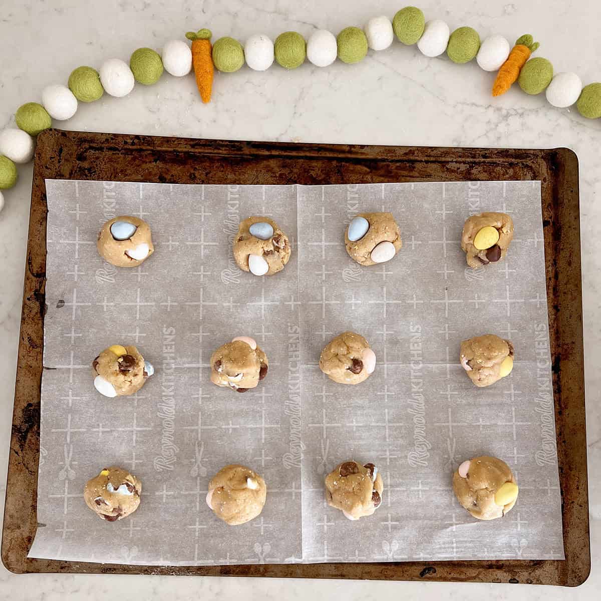 Balls of cookie dough with cadbury egg candies on a baking sheet.