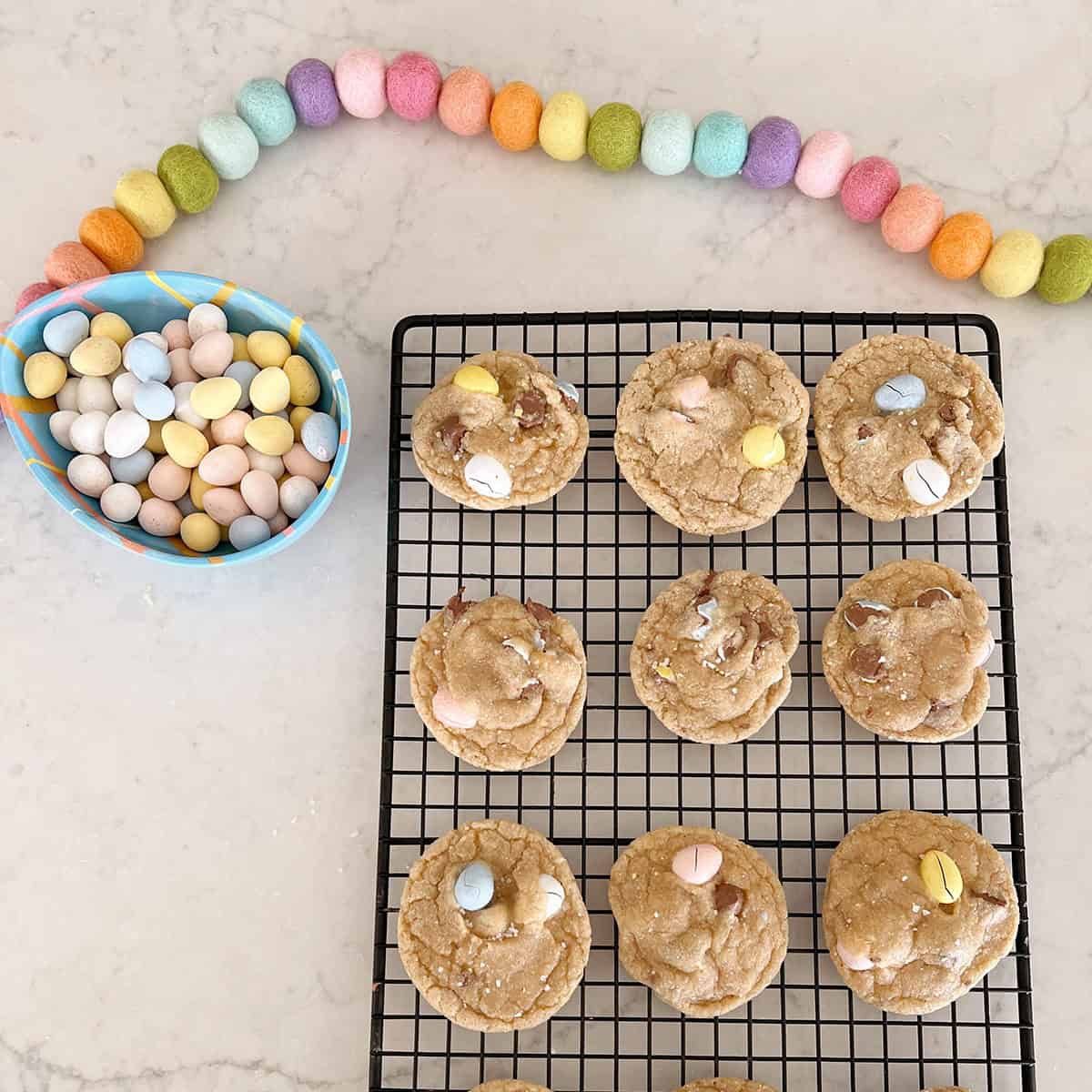 Chocolate chip cookies made with cadbury eggs sitting on a counter next to a bowl of the cadbury egg candies.