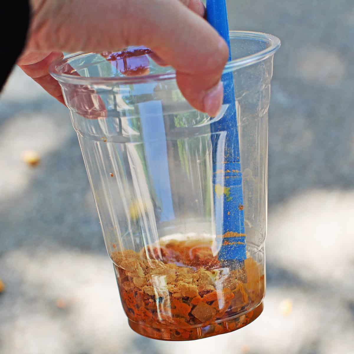 a clear plastic cup with chalk pieces and water being stirred.