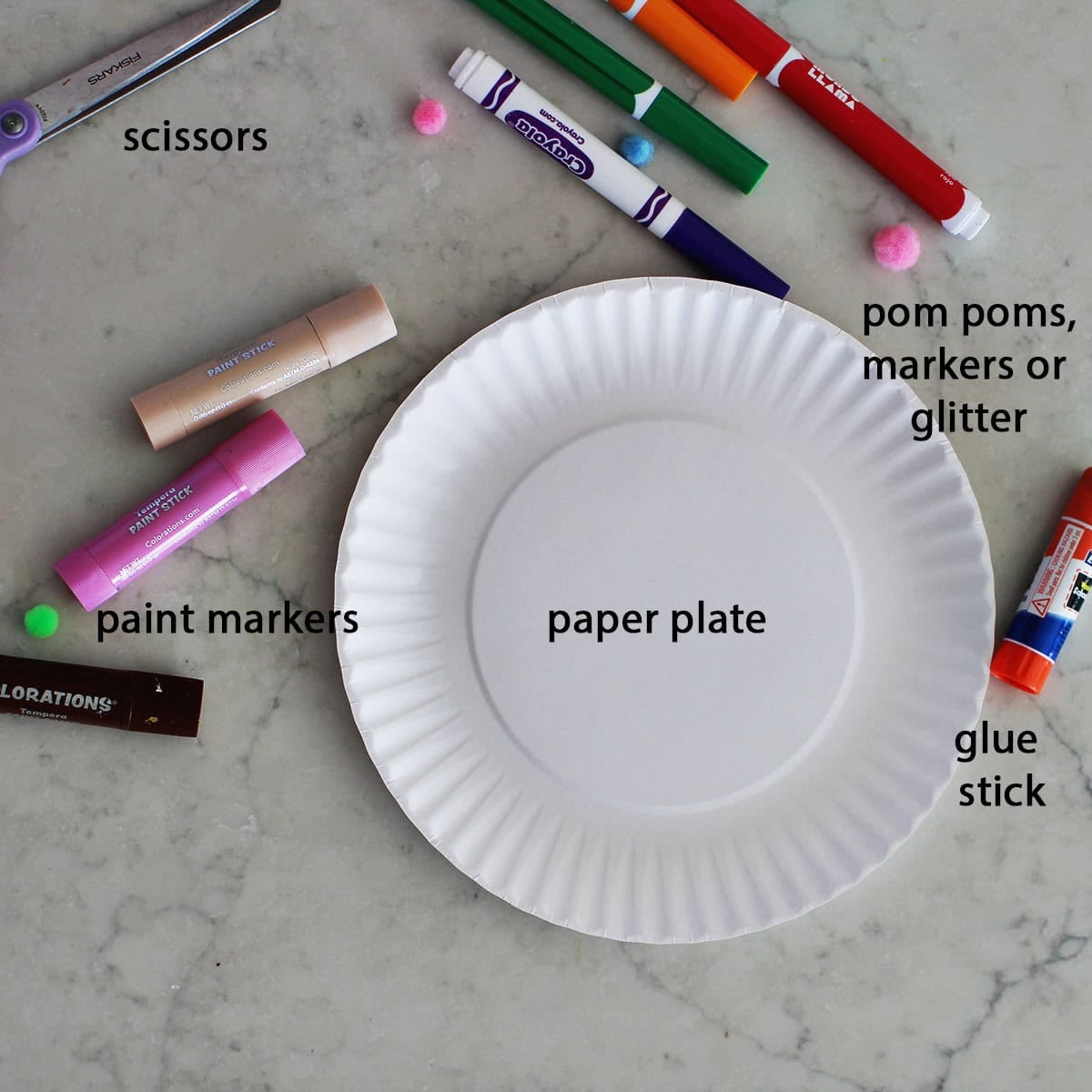 paper plate next to paint sticks, markers, and a glue stick on a counter.