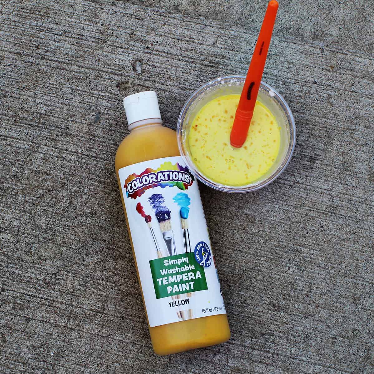 bottle of yellow paint next to a cup of water and paint with a paintbrush in it.