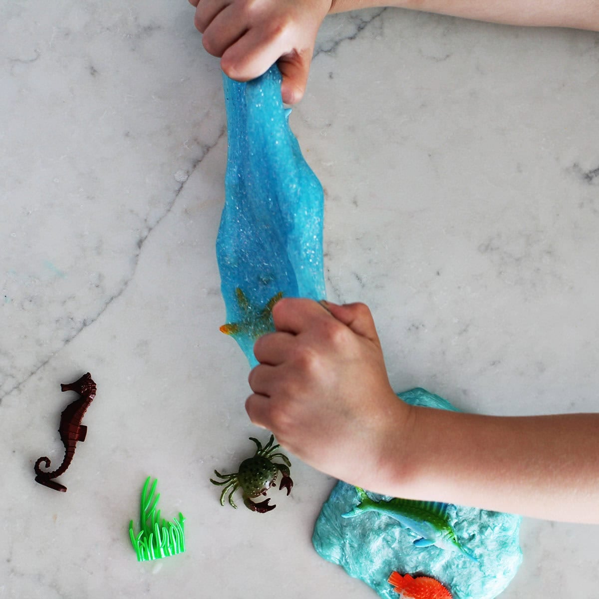 Kid's hands stretching slime on a counter.