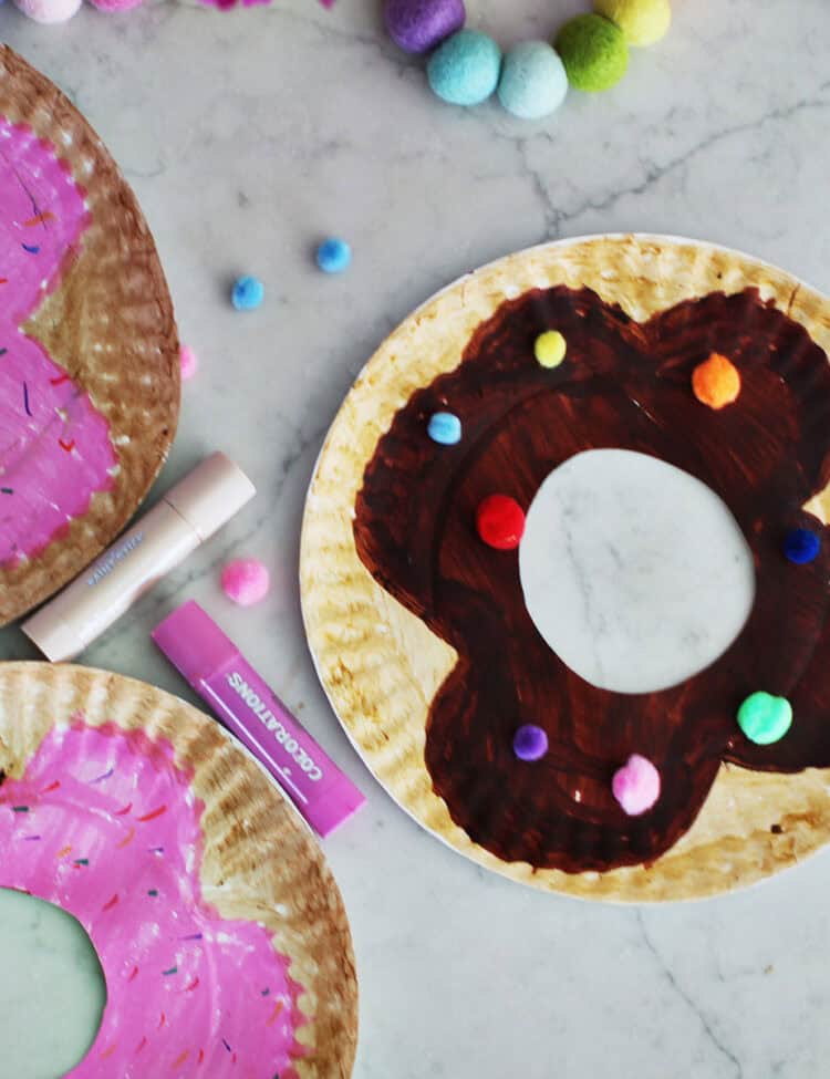 paper plates decorated with paint sticks and poms to look like donuts.
