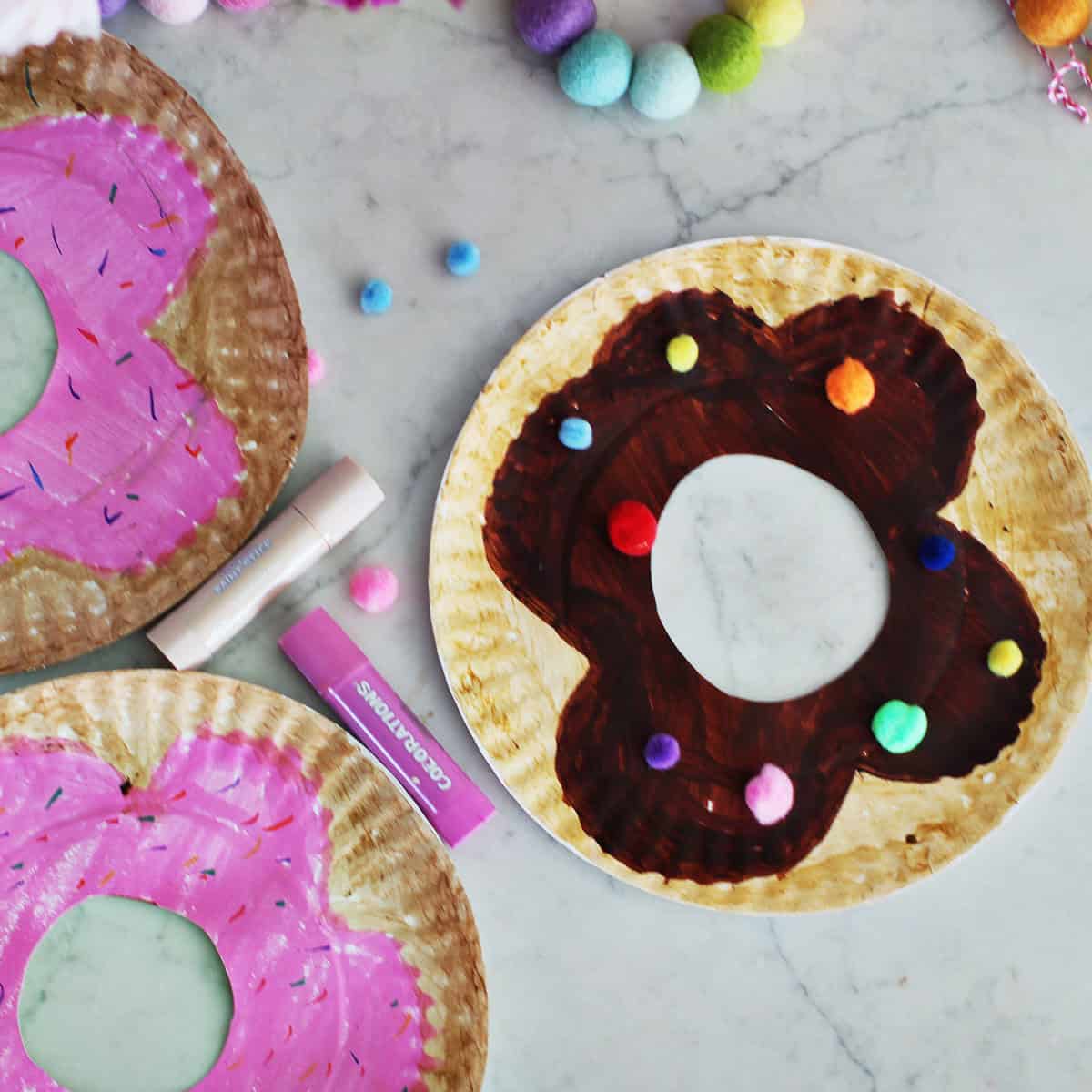 paper plates decorated with paint sticks and poms to look like donuts.