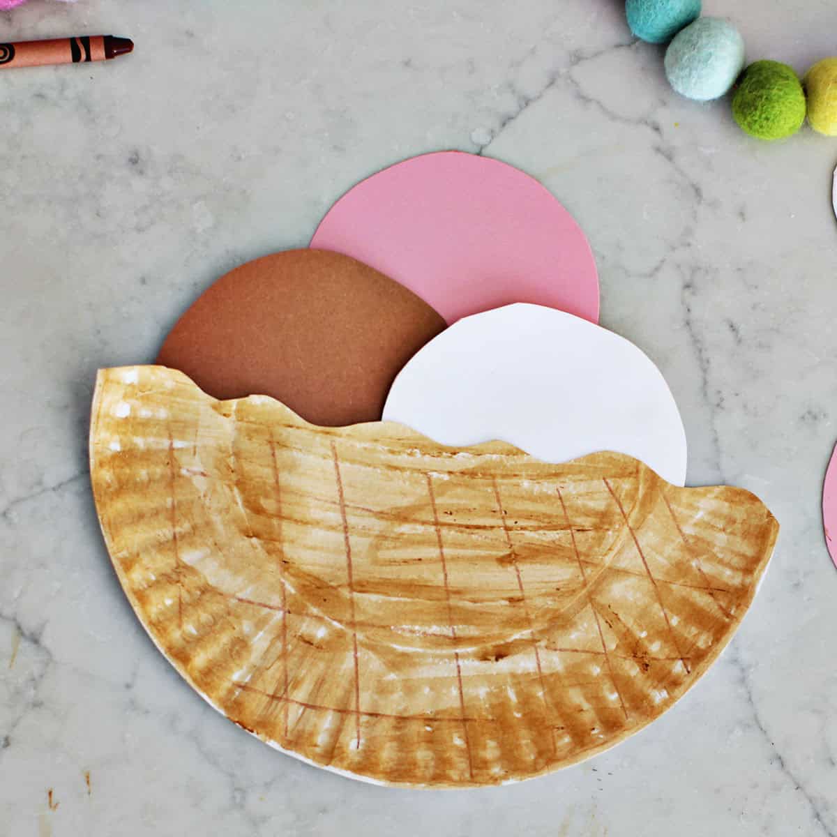 A pink, white and brown circle made from construction paper glued to half of a beige paper plate to look like ice cream.