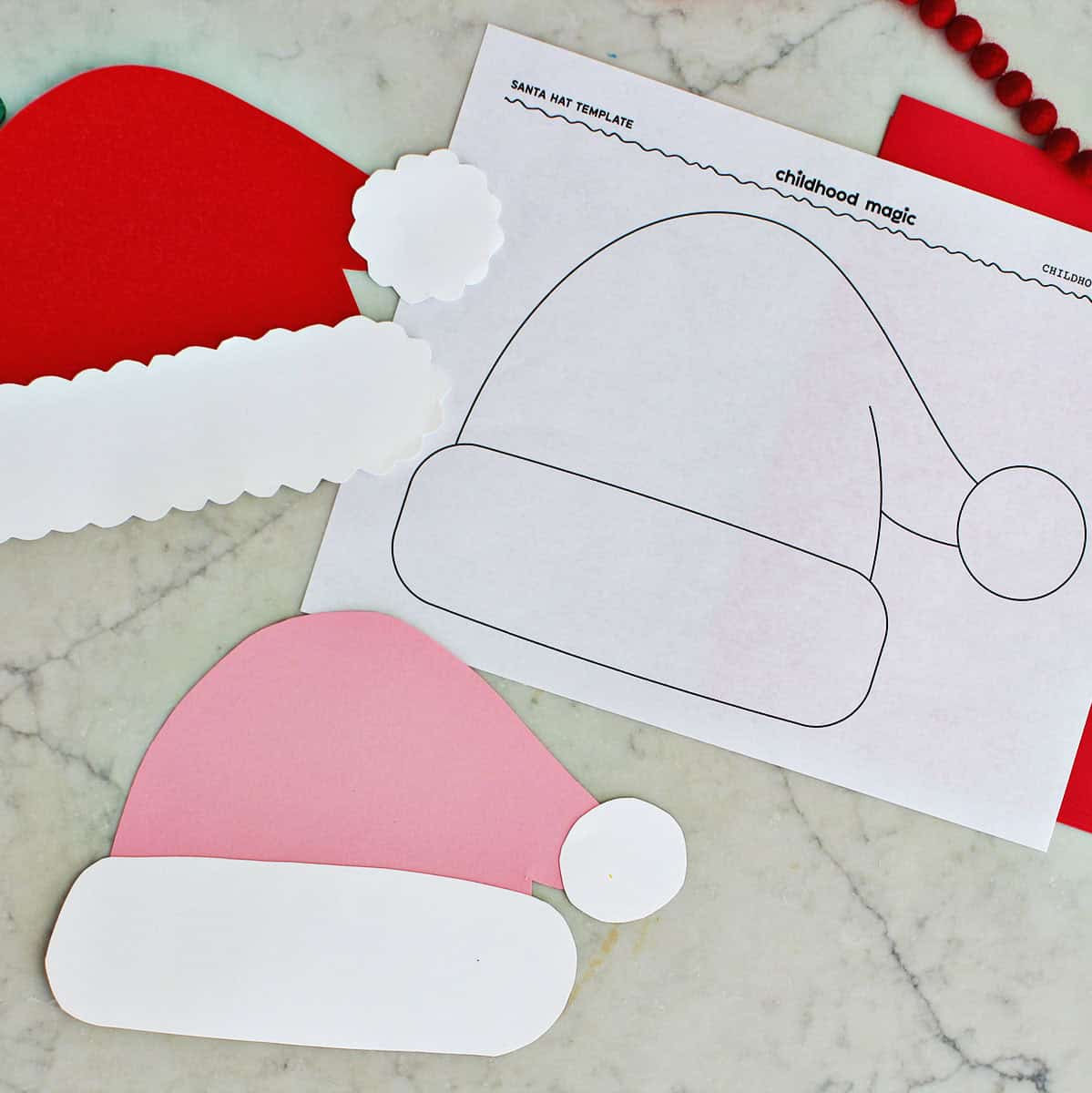 Page with santa hat template on it next to cut out santa hats made from cardstock paper.