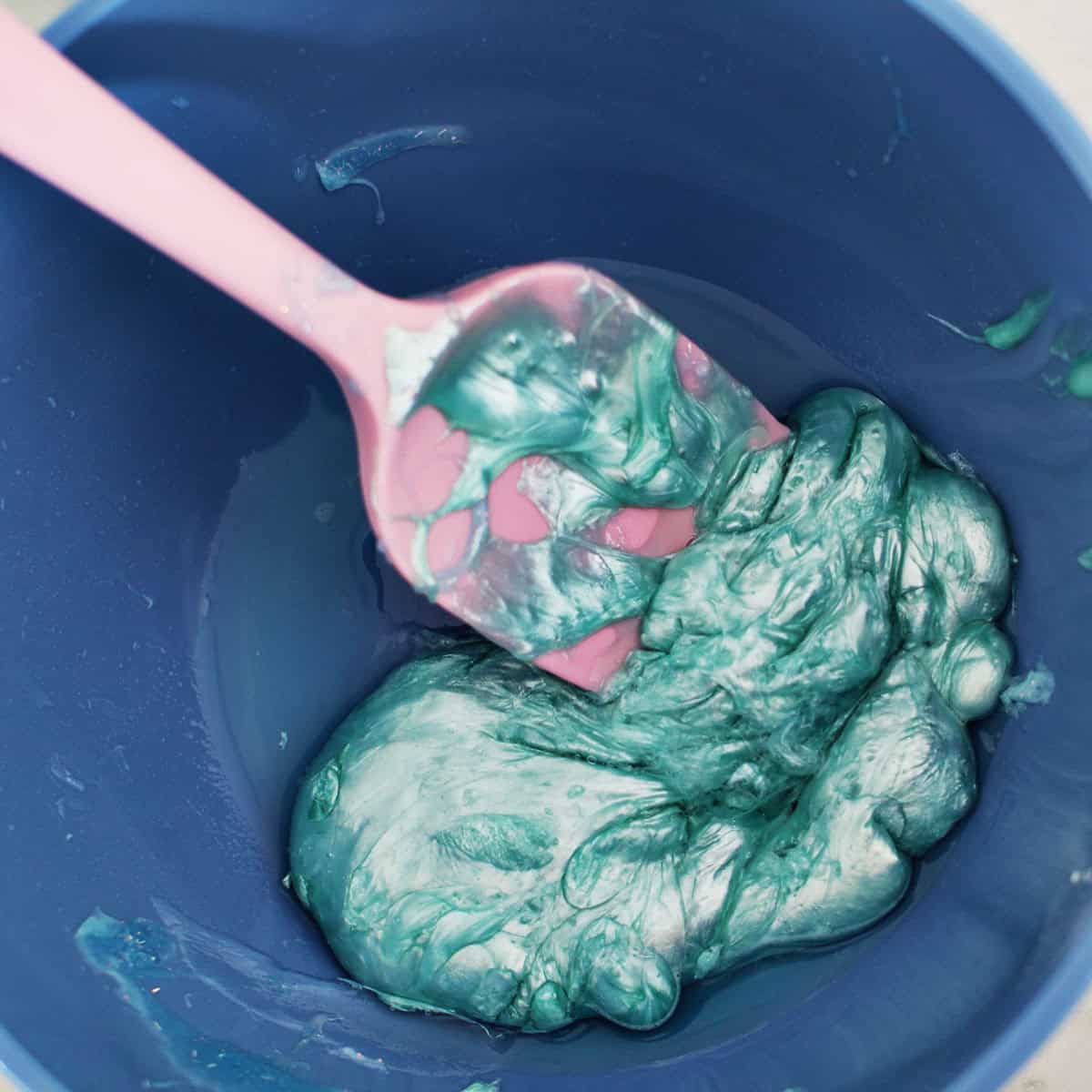 Metallic glue being stirred by a pink spatula in a blue bowl.